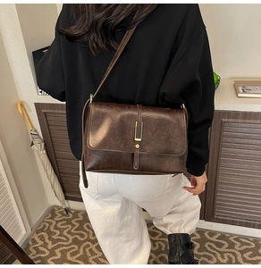 Détail d'un sac bandoulière vintage marron foncé avec boucle dorée et bandoulière fine