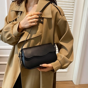 Vintage black leather shoulder bag with wavy flap design on a beige trench coat