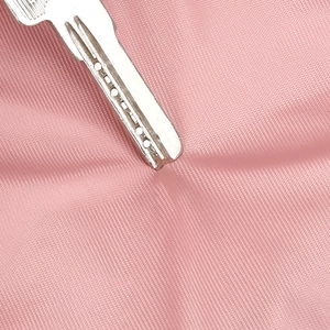 Macro shot of pink nylon chest bag fabric undergoing scratch resistance test with key