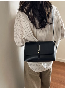 Détail d'un sac bandoulière en cuir noir mat avec boucle en métal doré et lanière
