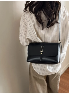 Gros plan d'un sac bandoulière noir avec boucle dorée sur une tenue minimaliste