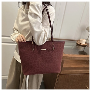 Detail of burgundy leopard embossed tote bag with gold logo plate and metal buckle