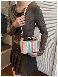 Detail of colorful striped woven crossbody bag showing compact size on female model