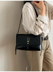 Detail of vintage black leather crossbody bag featuring gold U-shaped buckle and rivets