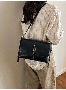 Détail d'un sac bandoulière en cuir noir avec ornements dorés sur une chemise à rayures