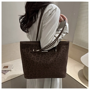 Detail of a large leopard print tote bag with slim shoulder straps and gold metal hardware