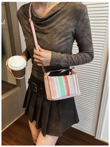 Close-up of a colorful woven crossbody box bag featuring pink leather sides and gold buckles