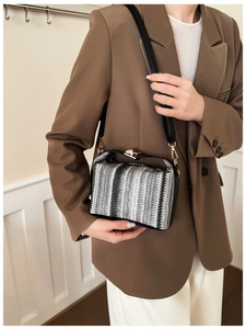 Détail du sac bandoulière tissé noir, blanc et gris avec ferrures dorées porté par un mannequin