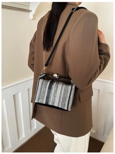 Detail of a striped woven box bag with metal twist lock and black shoulder strap on model
