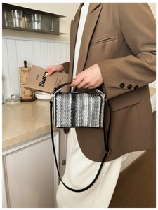 Detail of woven striped tote bag with thin black shoulder strap and gold hardware