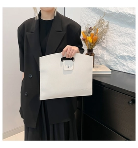 Close-up of white lychee leather laptop bag held by a model in a black blazer