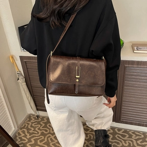 Sac bandoulière vintage en cuir huilé marron foncé avec boucle dorée sur modèle