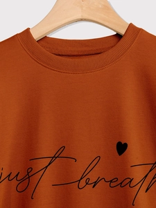 Close-up of ribbed crewneck on caramel sweatshirt with just breathe heart print