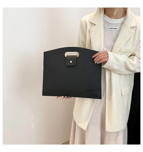 Detail of black pebbled leather handbag with handle held by model in beige blazer
