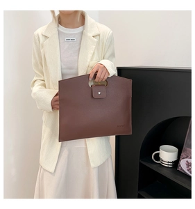 Detail of a brown leather document bag with a metal snap buckle and hollow handle