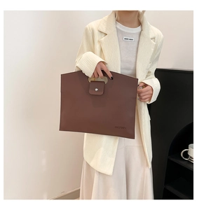 Detail of brown leather commuter tote bag with silver buckle and integrated handle