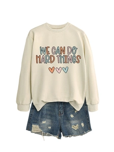 Détail de l'imprimé 'WE CAN DO HARD THINGS' sur sweat-shirt crème et short en denim bleu