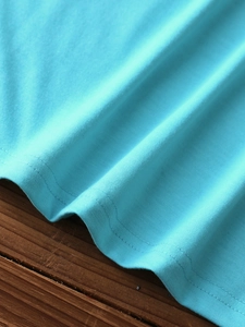 Detailed close-up of sky blue knitted vest showing hemline stitching on wood texture