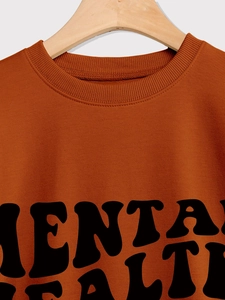 Close-up of burnt orange sweatshirt ribbed neckline and Mental Health letter print
