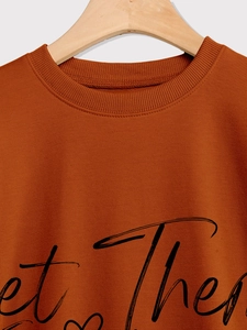 Detail of caramel crewneck sweatshirt with black let them cursive lettering on a wooden hanger