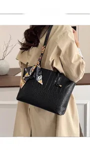 Detail of black crocodile embossed tote bag with silk scarf on handle, worn with beige coat