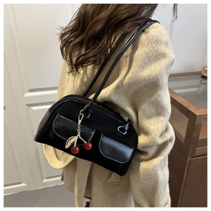 Detail of black retro shoulder bag with dual pockets and red cherry charm on beige coat