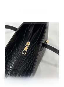 Detail of smooth gold metal zipper on black crocodile pattern leather handbag