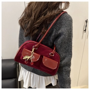 Detail of burgundy baguette bag with cherry charm and plush texture on a female model