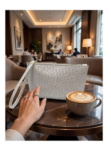 Detail of white woven leather clutch bag with wrist strap on a marble table with coffee