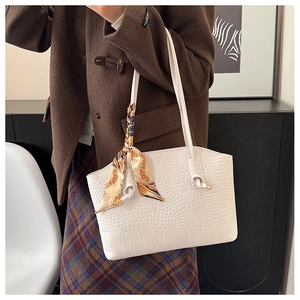 Detail of white crocodile-embossed tote bag with decorative silk scarf on the handle