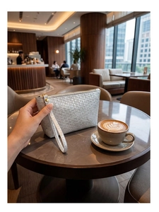 Close-up of a silver woven envelope clutch bag on a marble table in a cozy cafe setting