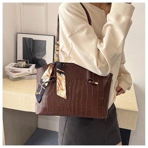 Detail of elegant dark brown crocodile embossed leather tote bag with silk scarf on handle