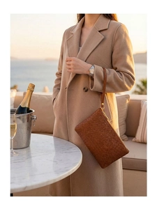Detail view of a caramel brown woven leather clutch with gold zipper in a luxury setting