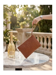 Detailed texture of brown woven leather clutch with a wristlet strap in a sunlit outdoor setting