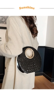 Detail of elegant black crocodile embossed handbag with large gold round metal handle