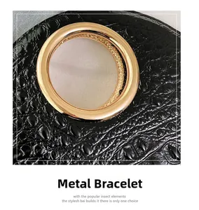 Detail of a black croc-embossed leather bag featuring a polished gold circular metal handle