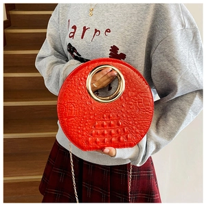Detail of red crocodile pattern circular handbag with a large gold metal ring handle