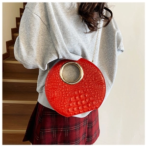 Detail of red crocodile texture handbag with golden circular handle and metal chain