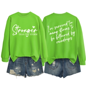 Flat lay of neon green Stronger Than The Storm sweatshirt with ripped denim shorts