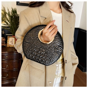 Close-up of black crocodile pattern handbag with large round gold metal handle on model