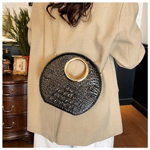 Detail of black faux crocodile leather bag featuring a bold gold circular ring and chain strap