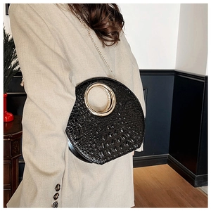 Detail of black crocodile texture bag with large gold metal ring handle and chain strap