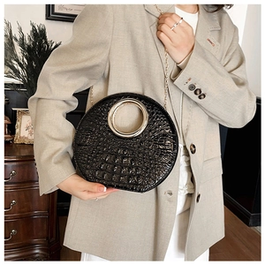 Detail of black crocodile texture bag with gold metal ring handle and chain strap