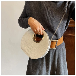 Detail of cream round handbag featuring crocodile texture and gold circular handle
