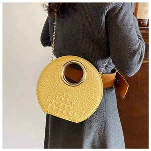 Detail of yellow crocodile embossed handbag with gold circular handle and chain strap