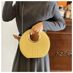 Detail of yellow round handbag with crocodile texture, gold ring handle and chain strap