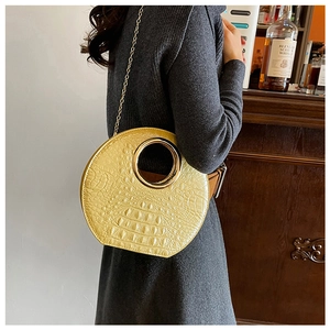 Detail of yellow crocodile embossed leather bag with golden circular metal handle
