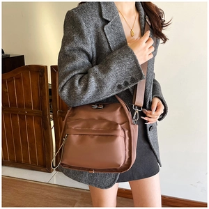 Detail of dark brown nylon multi-layer crossbody bag worn with a gray blazer
