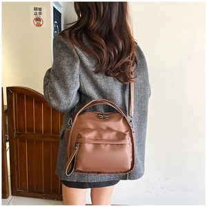 Detail of waterproof dark brown oxford fabric backpack worn by a model in casual setting