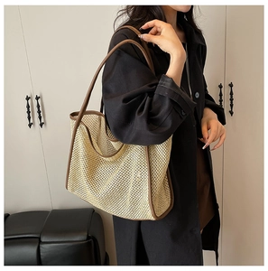 Chic straw woven tote bag with brown leather trim carried by a model in a minimalist setting